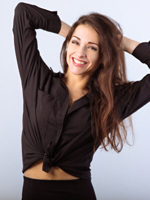 Happy toothy enjoying smiling woman posing in black shirt standing and holding hands behind the head on studio blue background with empty copy space. Closeup front classic banner portrait